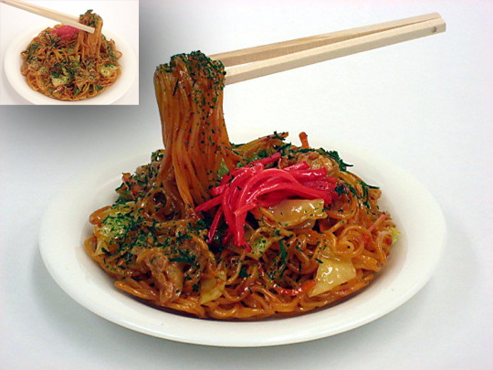 A model of a plate of yakisoba noodles, with a pair of chopsticks suspended in mid-air