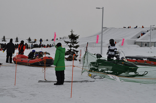 A rubber dingey about to be towed by a snowmobile and snow slides