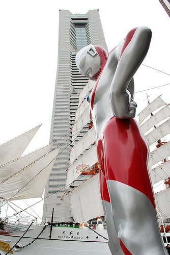 A giant replica of Ultraman stands in front of the Nippon Maru sailing boat and Landmark Tower in Yokohama