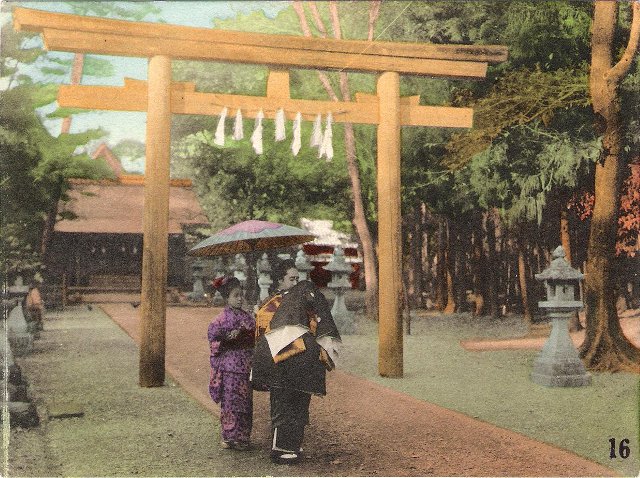 Two people stand in front of the tori gate of a Japanese Shinto shrine, one carrying a parasol